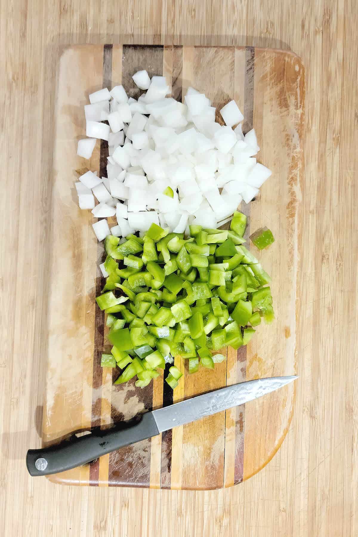 Chopped onions and green bell pepper on a cutting board.
