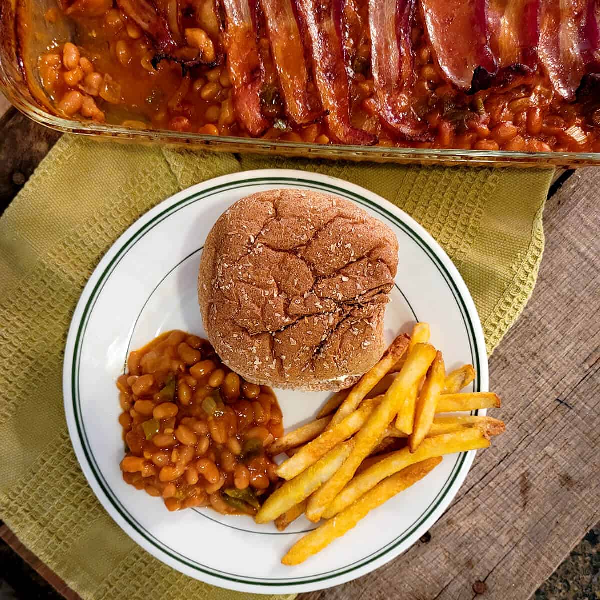 Baked beans and bacon on a plate with a hamburger and fries.