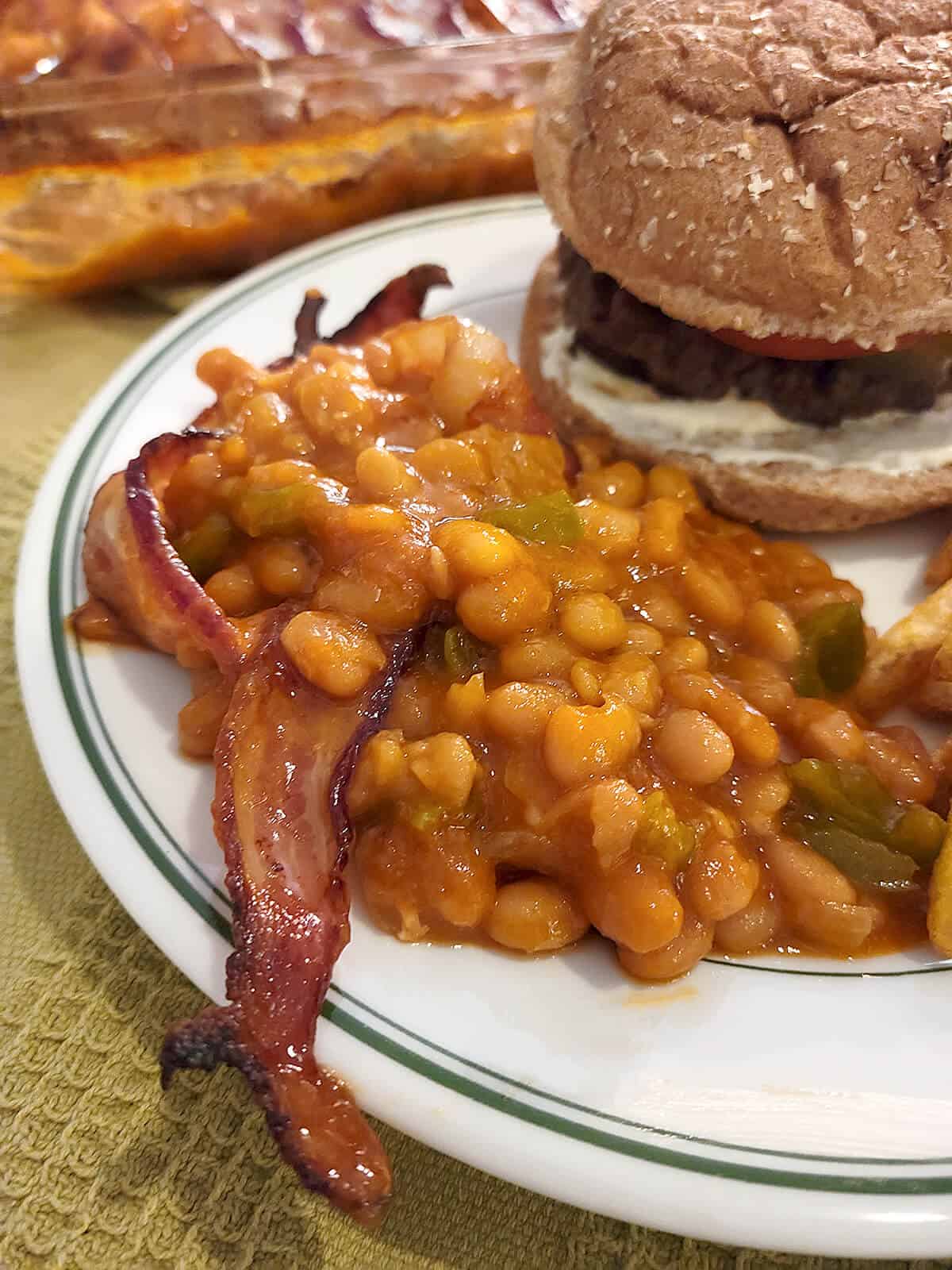 Baked beans and bacon on a plate with a hamburger.