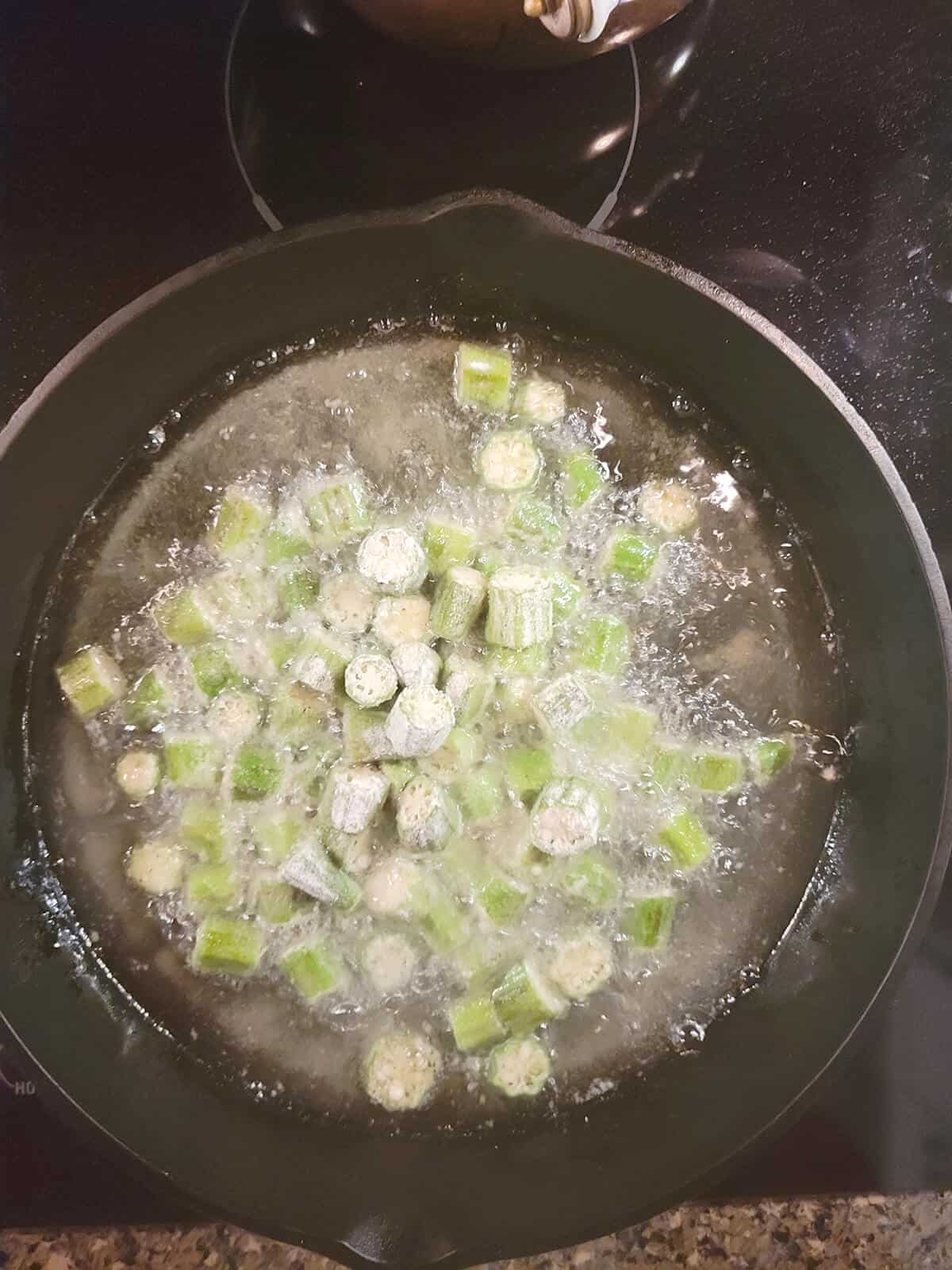 Okra added to the hot oil in a frying pan.