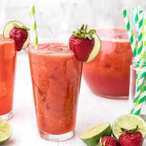 Two glasses of strawberry lemon limeade with a pitcher in the background.