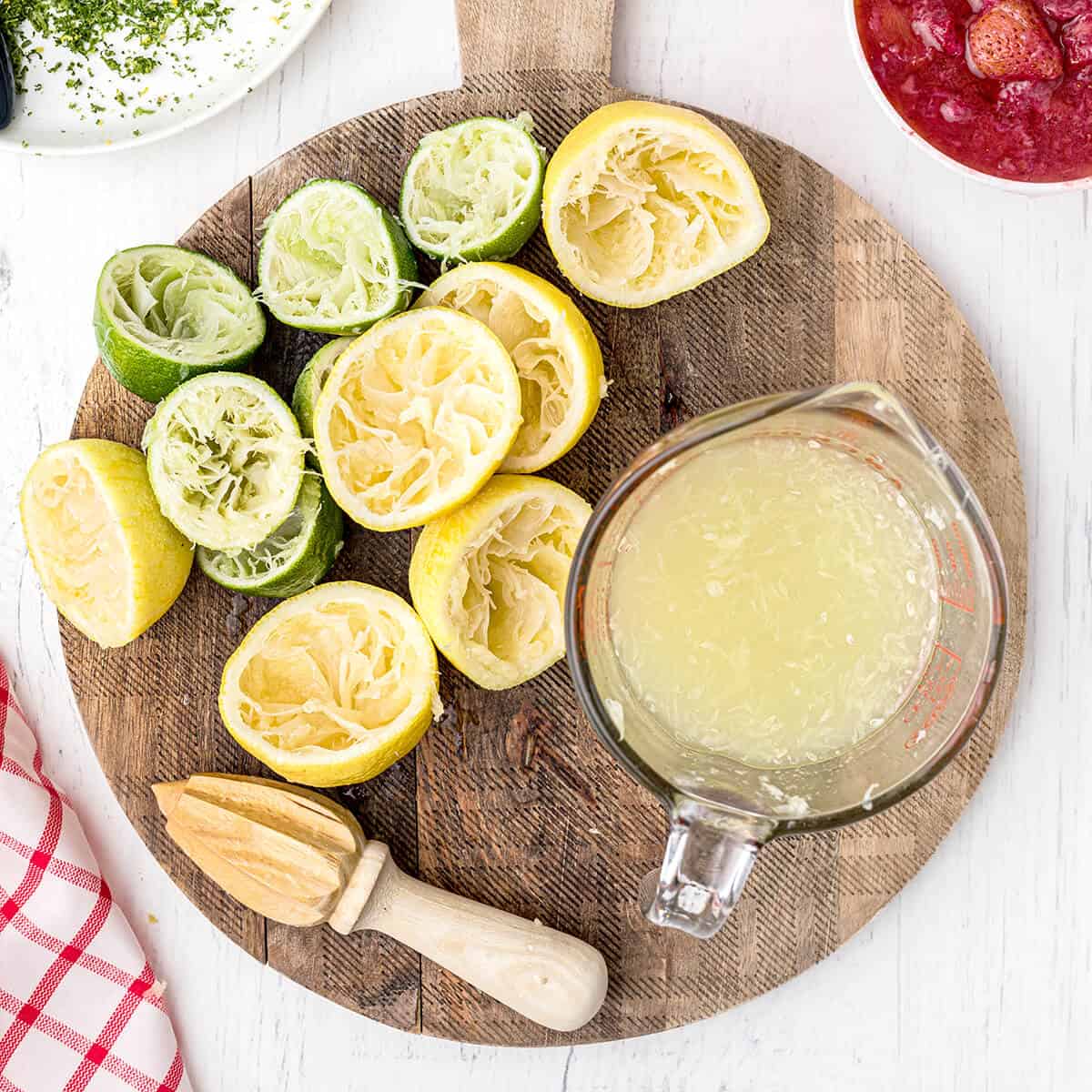 Lemon and lime halves on a board with a cup of juice and a reamer.