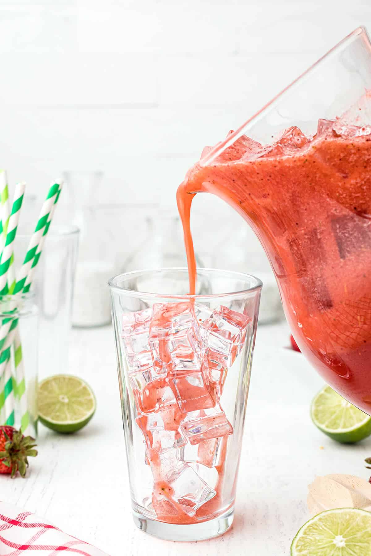 Strawberry lemon limeade being poured from a pitcher into a glass filled with ice.