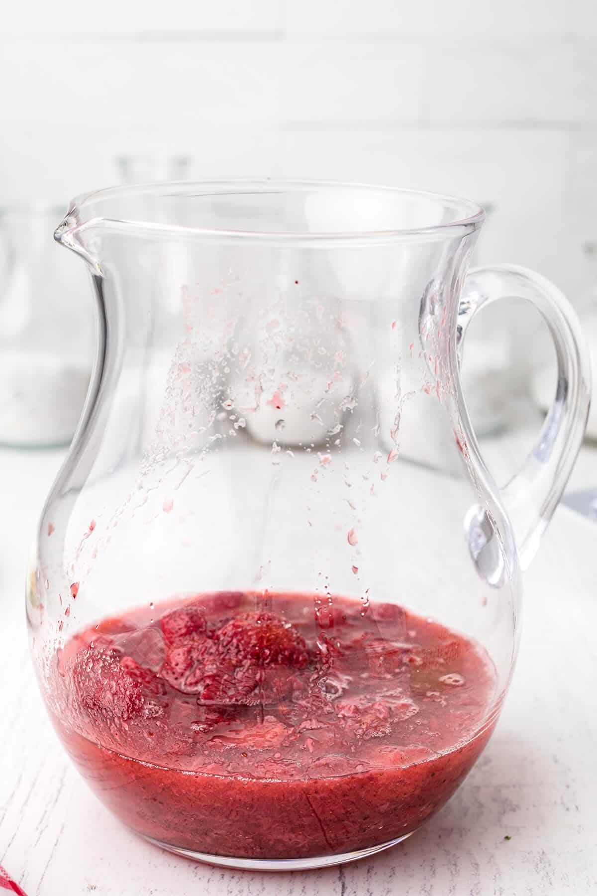 Thawed frozen strawberries in a glass pitcher.