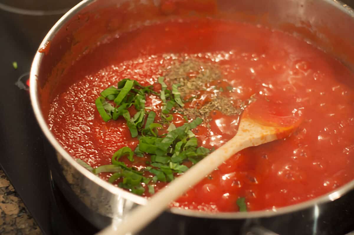 Adding tomatoes and seasonings to the sauce.