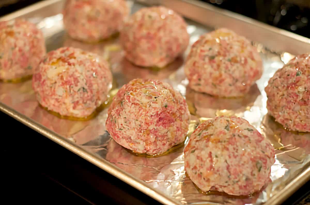 Meatballs on a baking sheet drizzled with olive oil.