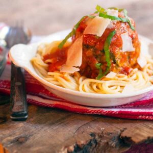 A serving of jumbo meatballs and spaghetti in a white bowl.