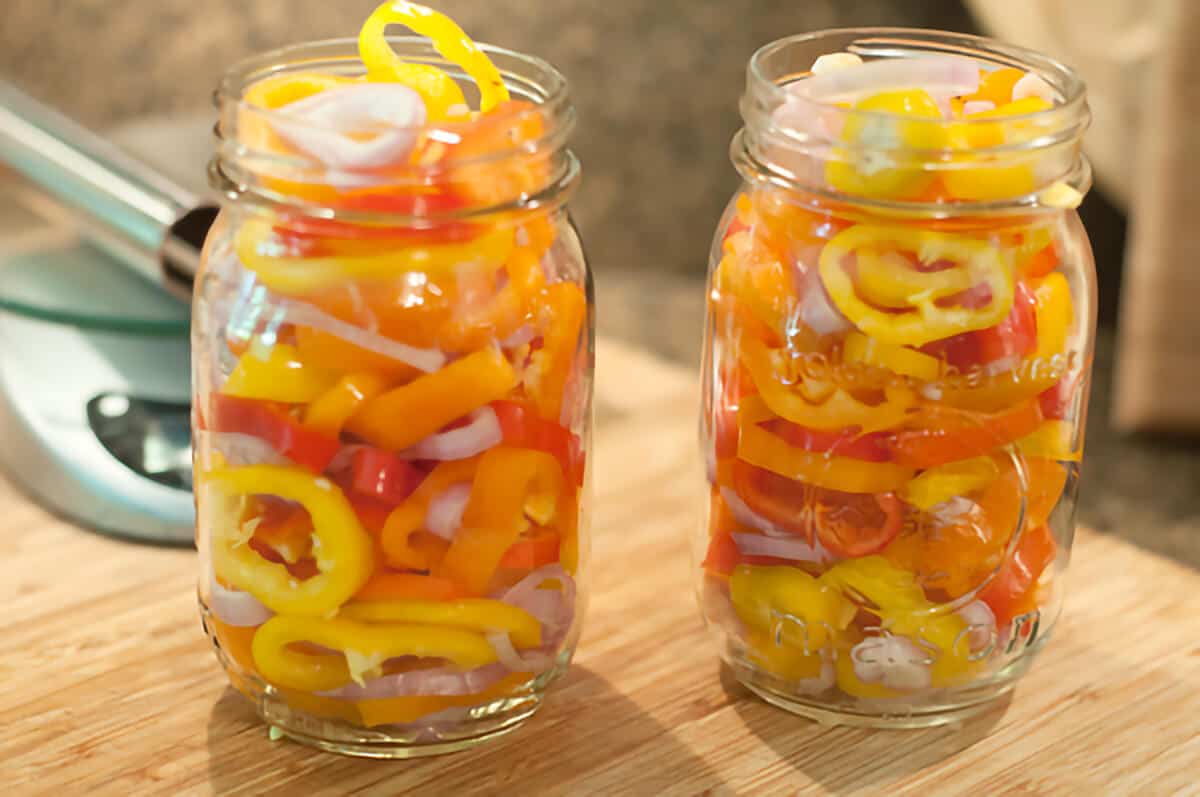 Sliced peppers and shallots packed into two glass jars.