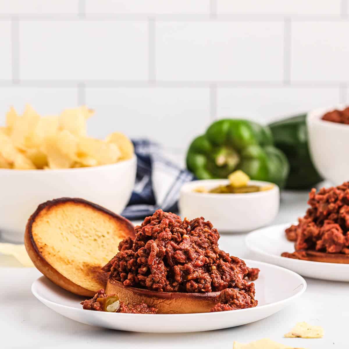 Assembled sloppy joe sandwich on a serving plate with pickles and chips.