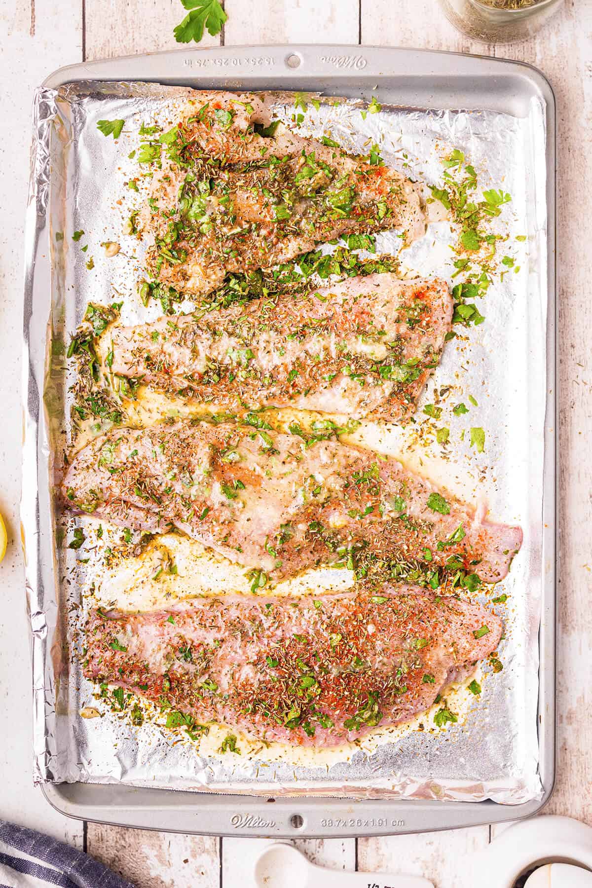 Seasoned catfish fillets on foil-lined pan drizzled with lemon-butter mixture.
