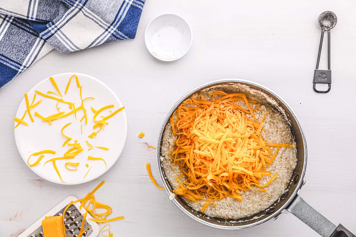 Small saucepan with cooked grits and grated cheese on top.