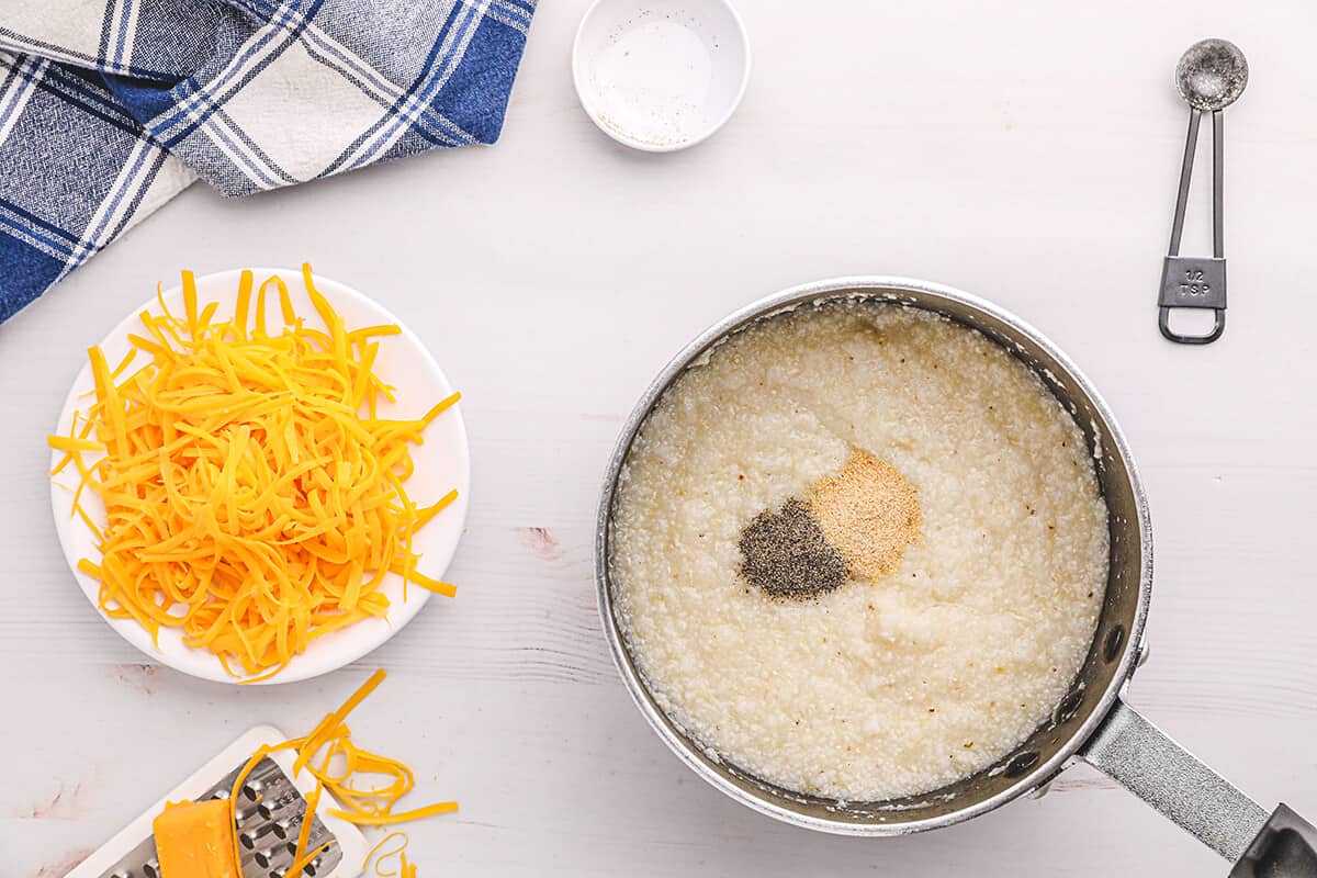 Small saucepan with cooked grits and seasonings added on top.