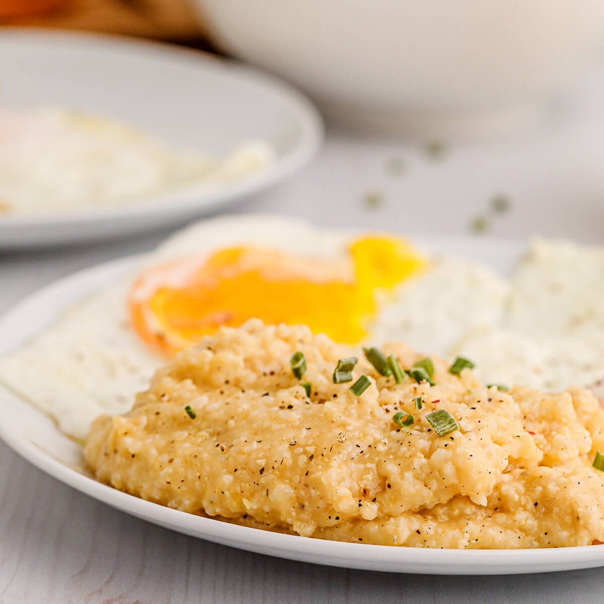 A white plate with a serving of cheese grits and over easy eggs.