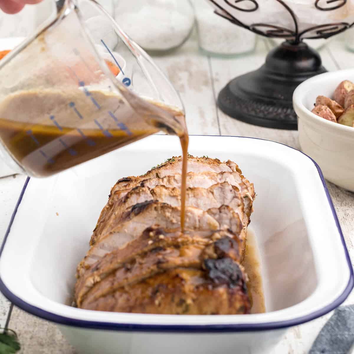 Pouring sauce over finished pork loin in a serving dish.