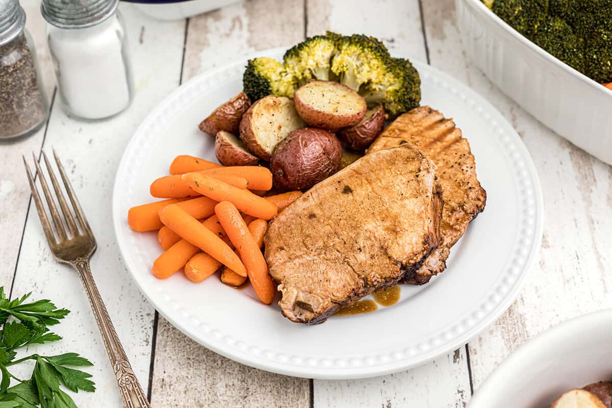 Sliced pork loin on a serving plate with vegetables on the side.