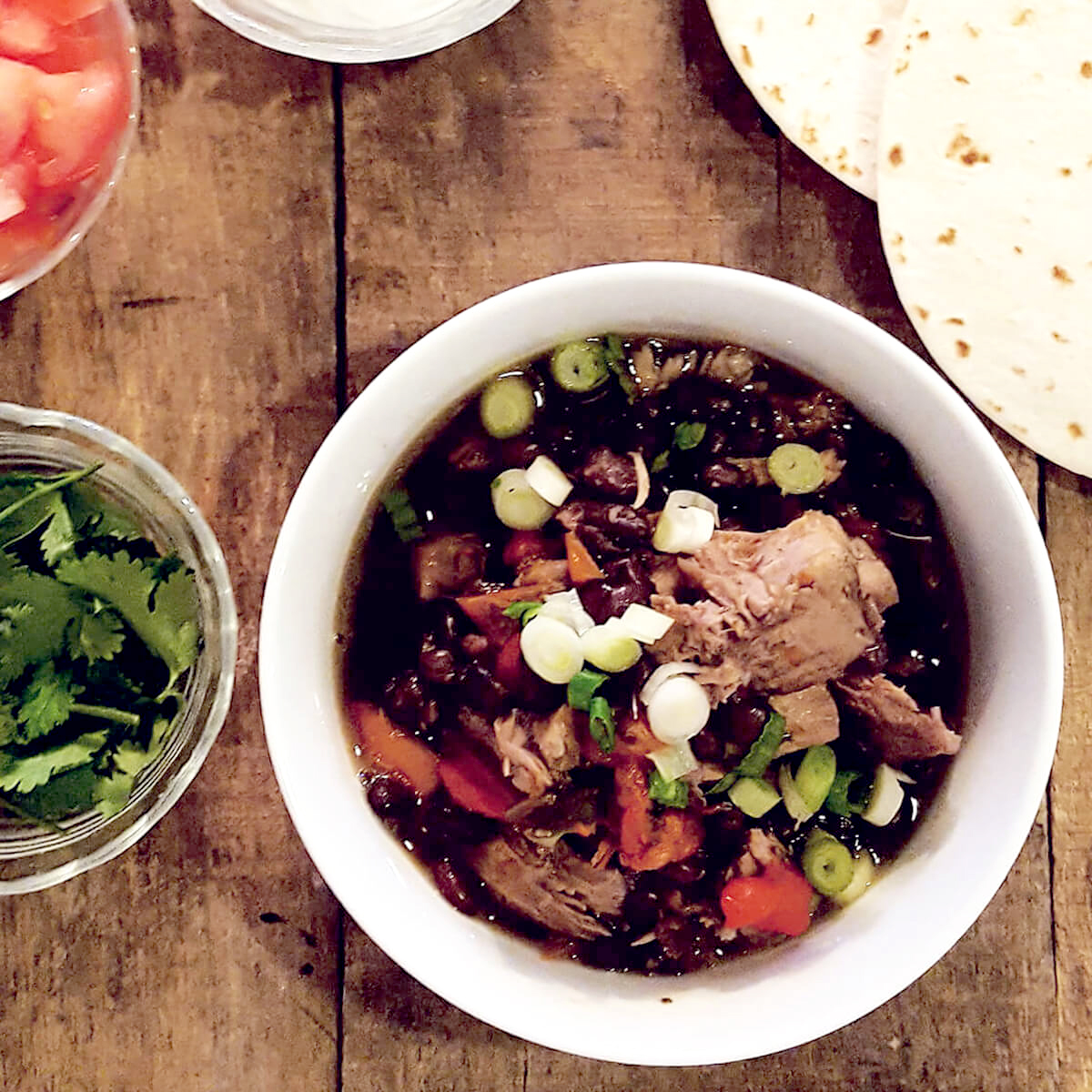 Slow Cooker Pork and Black Bean Stew in a serving bowl with garnishes on the side.