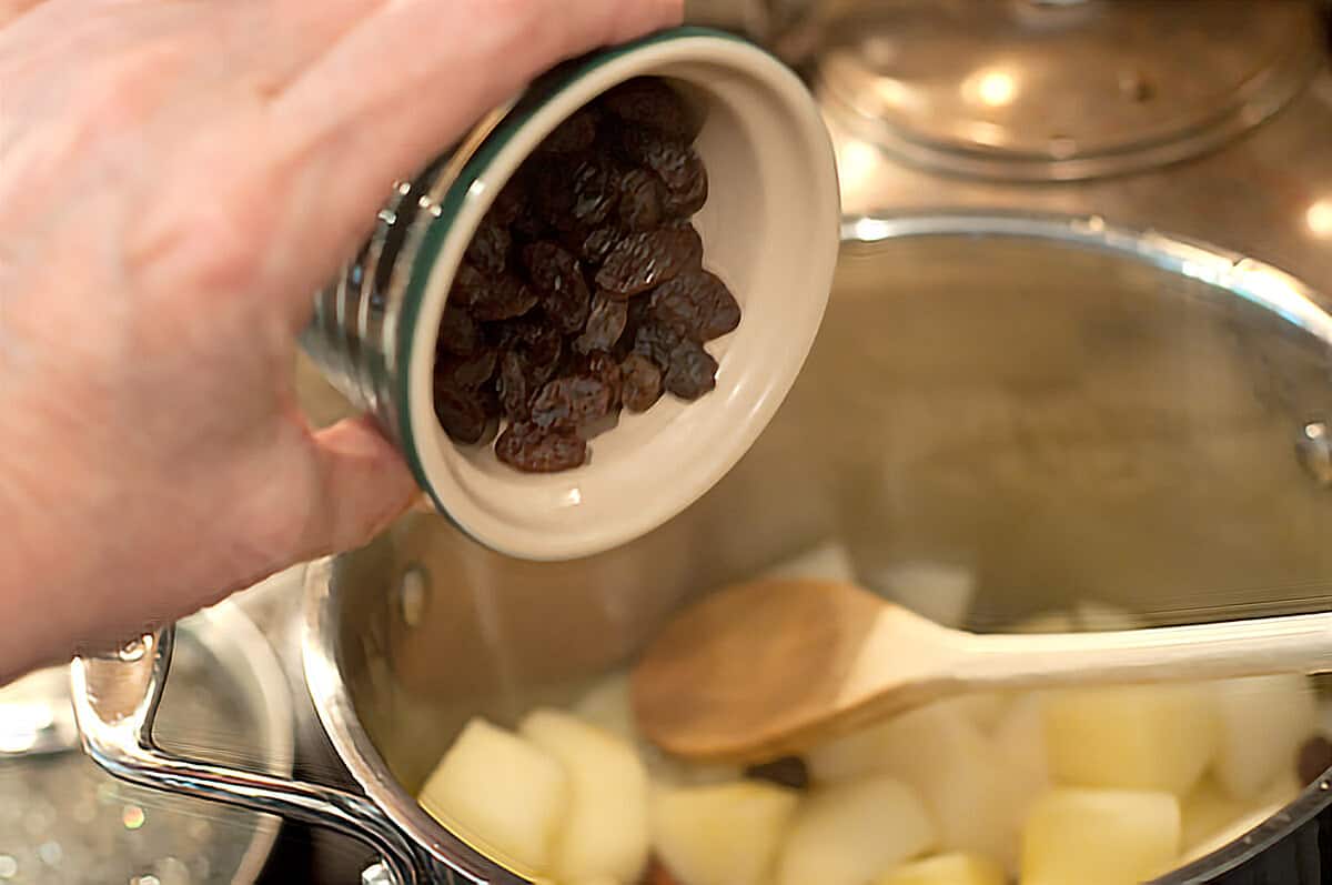 Adding raisins to the partially cooked fruit.