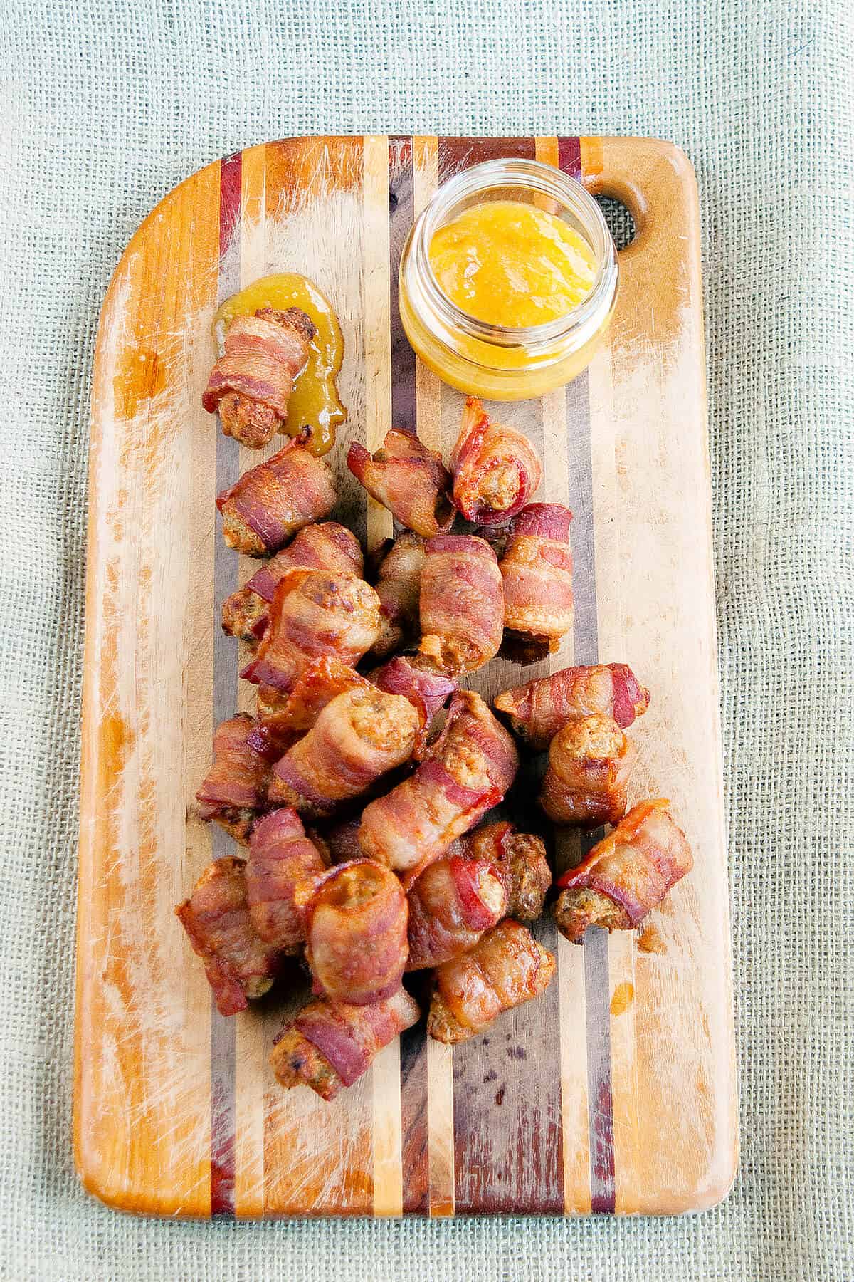 Bacon wrapped sausage balls and dipping sauce on a wooden board.