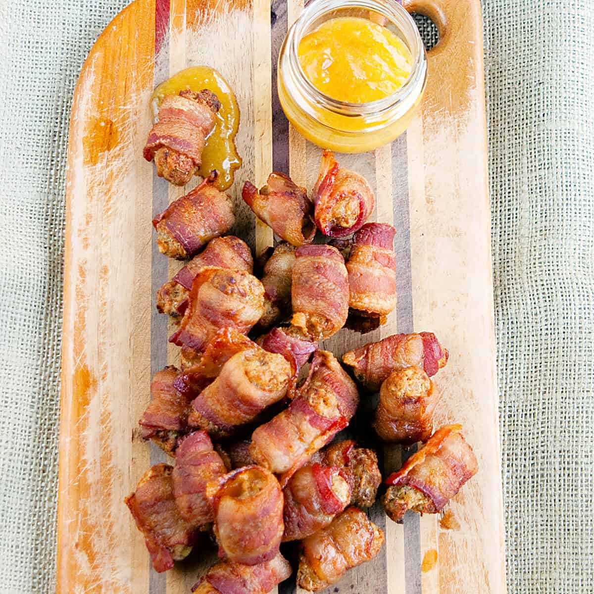 Bacon wrapped sausage balls and dipping sauce on a wooden board.