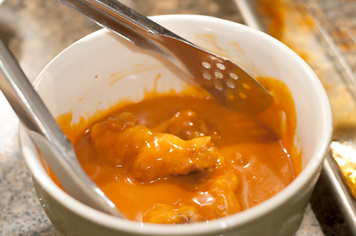 Tossing cooked wings in the sauce in a bowl.