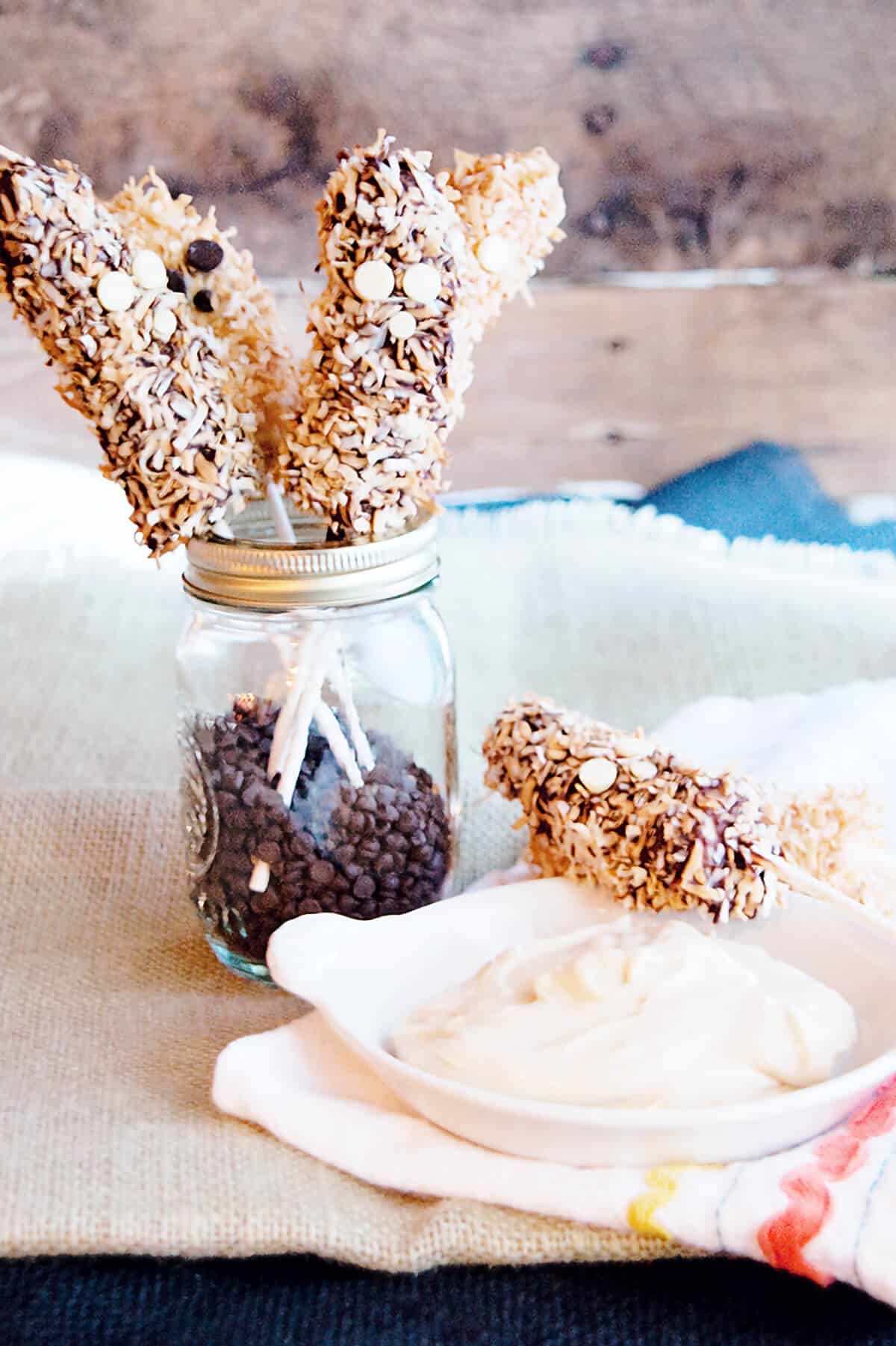 Banana pops in a jar with a bowl of cream cheese dip.