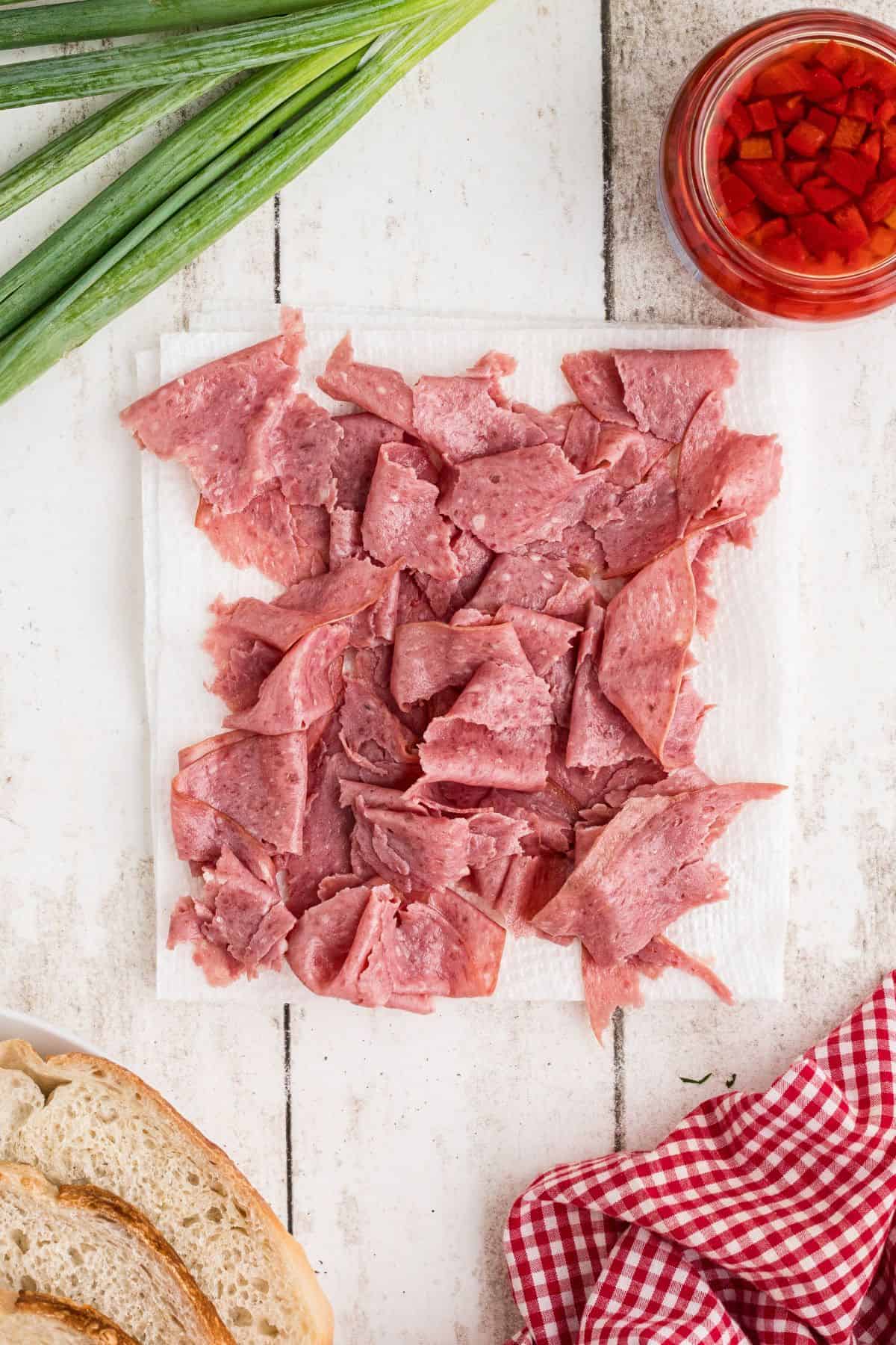 Beef torn into strips on paper towels pictured with the bread, pimento pieces, and green onions on the side.