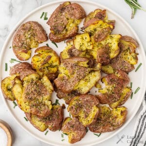 A plate of smashed roasted potatoes garnished with chopped herbs and coarse salt.