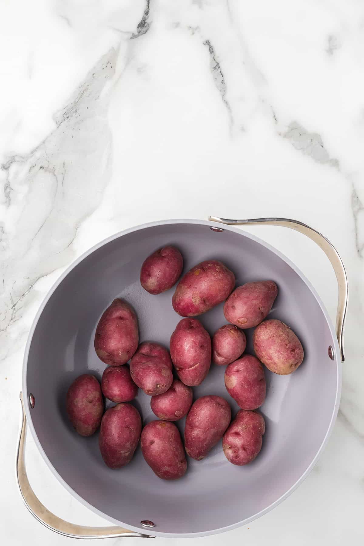 A gray pot with red potatoes sits on a white marble surface.