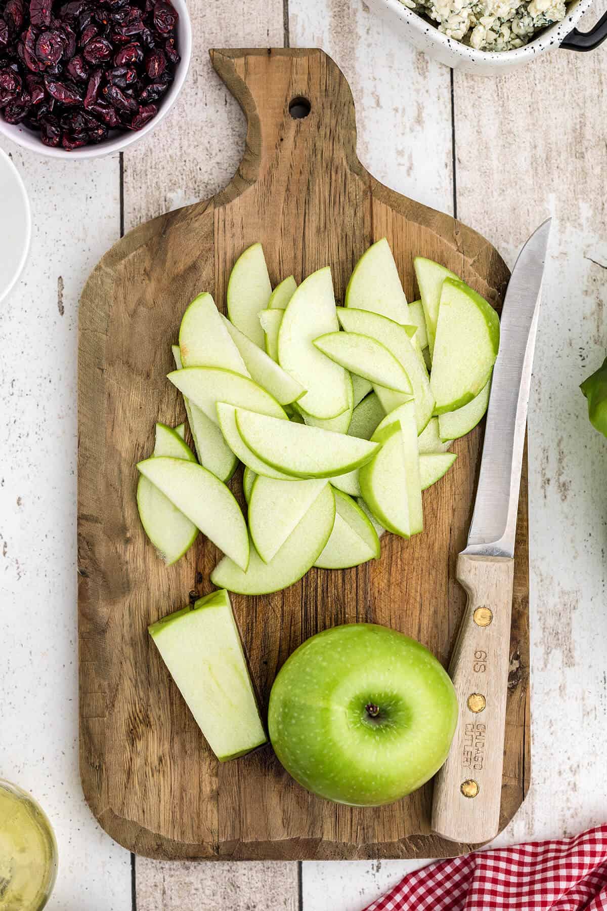 Apple slices and a knife on a cutting board.