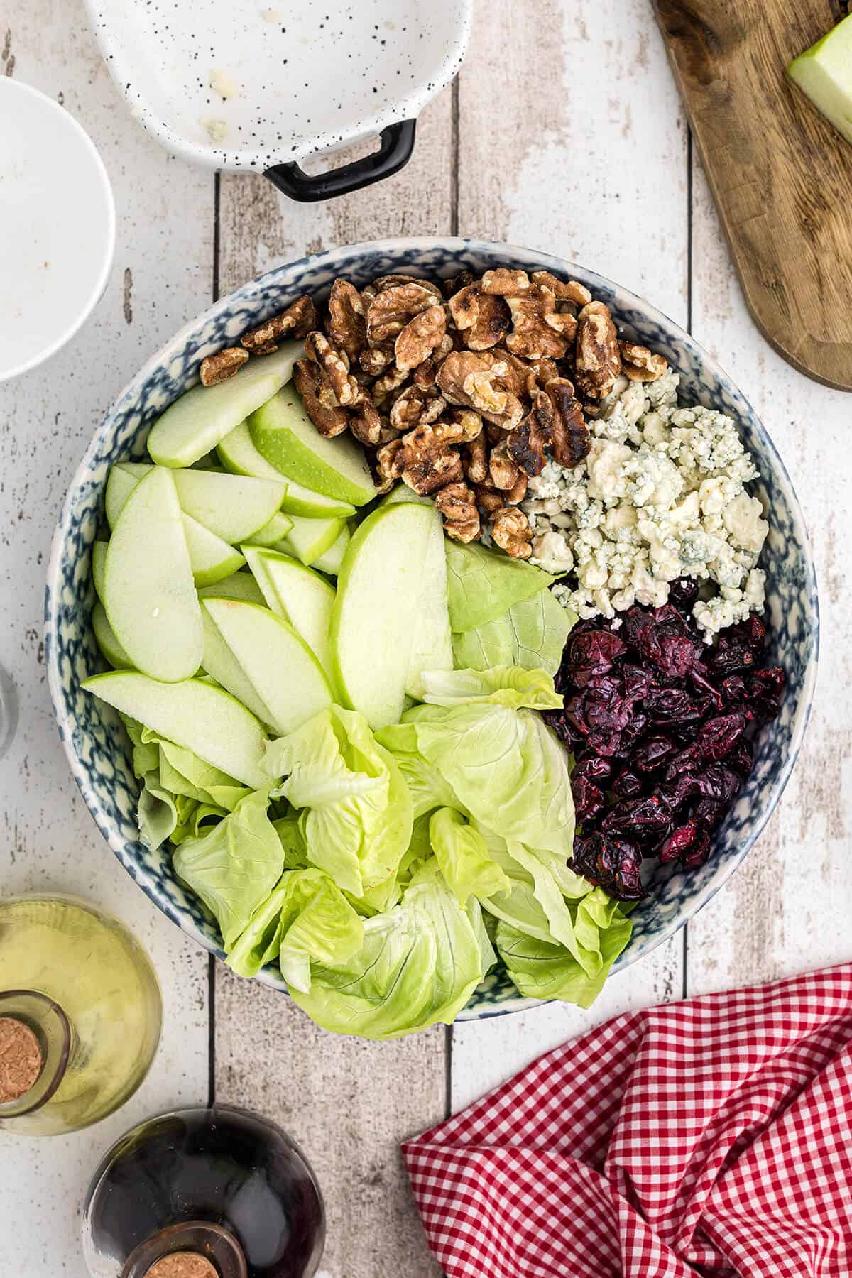 Apples, cranberries, lettuce, walnuts, and blue cheese in a bowl.