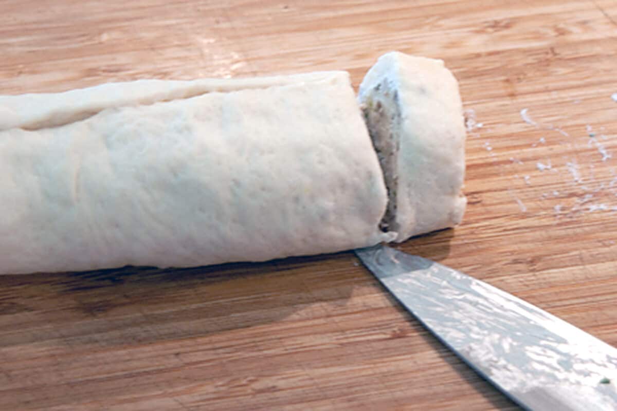 Filled, rolled pizza crust being sliced into rounds.