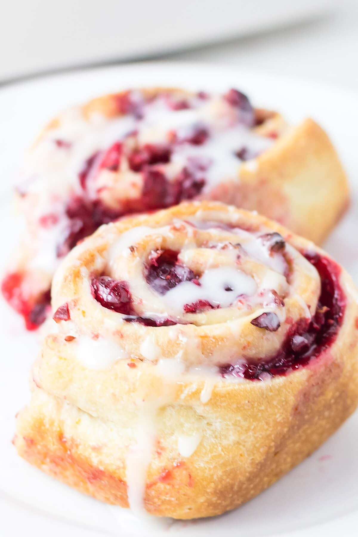 Finished cranberry orange sweet rolls with sugar glaze on a white serving plate.