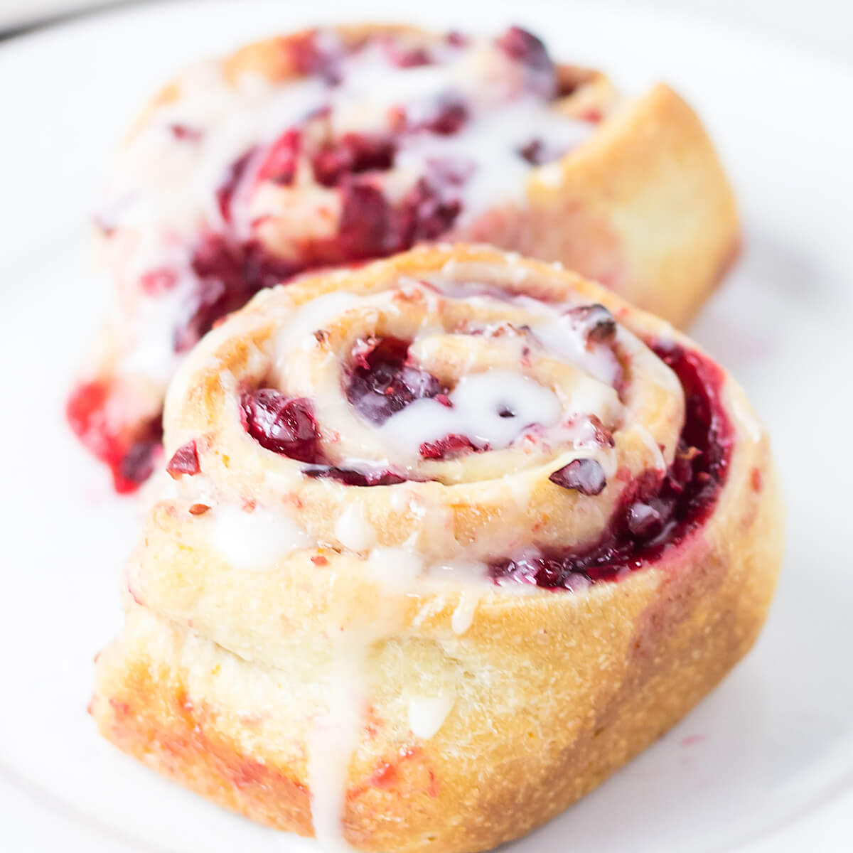 Finished cranberry orange sweet rolls with sugar glaze on a white serving plate.