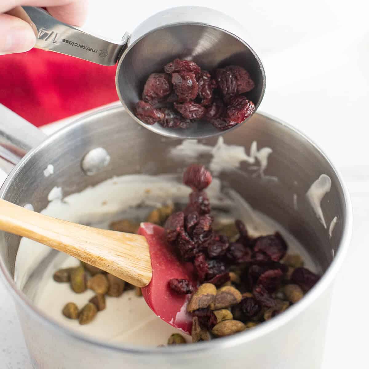 Cranberries and pistachios added to melted chocolate in a saucepan.