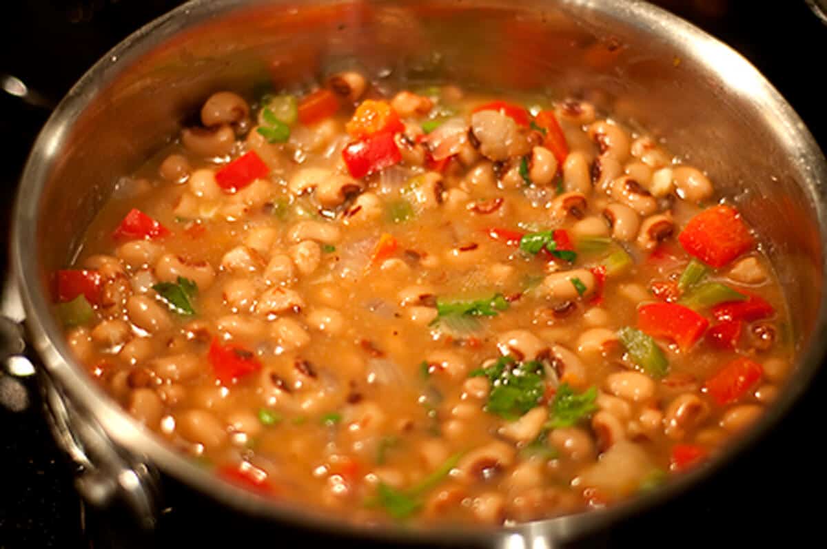 Adding blackeyed peas to vegetables in a skillet.
