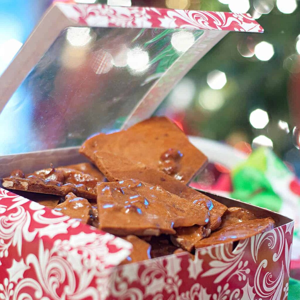 Peanut brittle in a candy gift box with Christmas tree lights in the background.