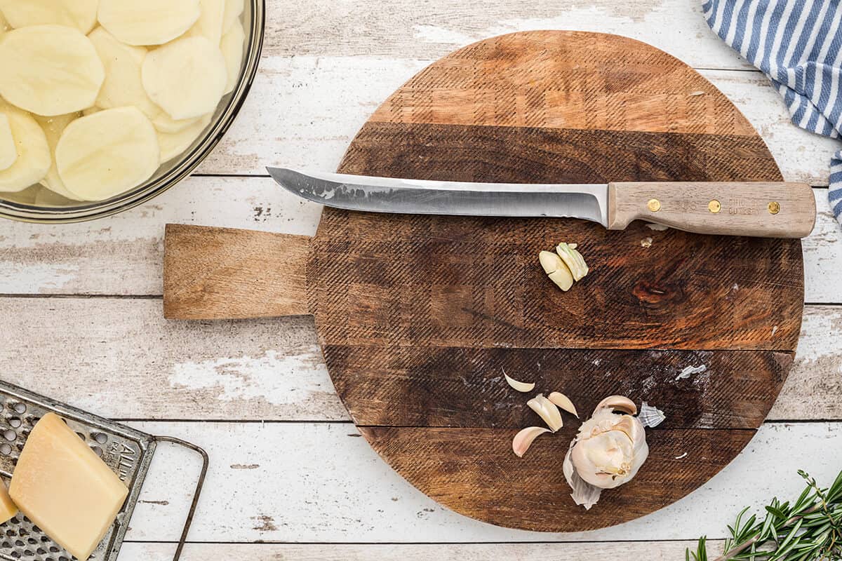 A knife and crushed garlic cloves on a cutting board.