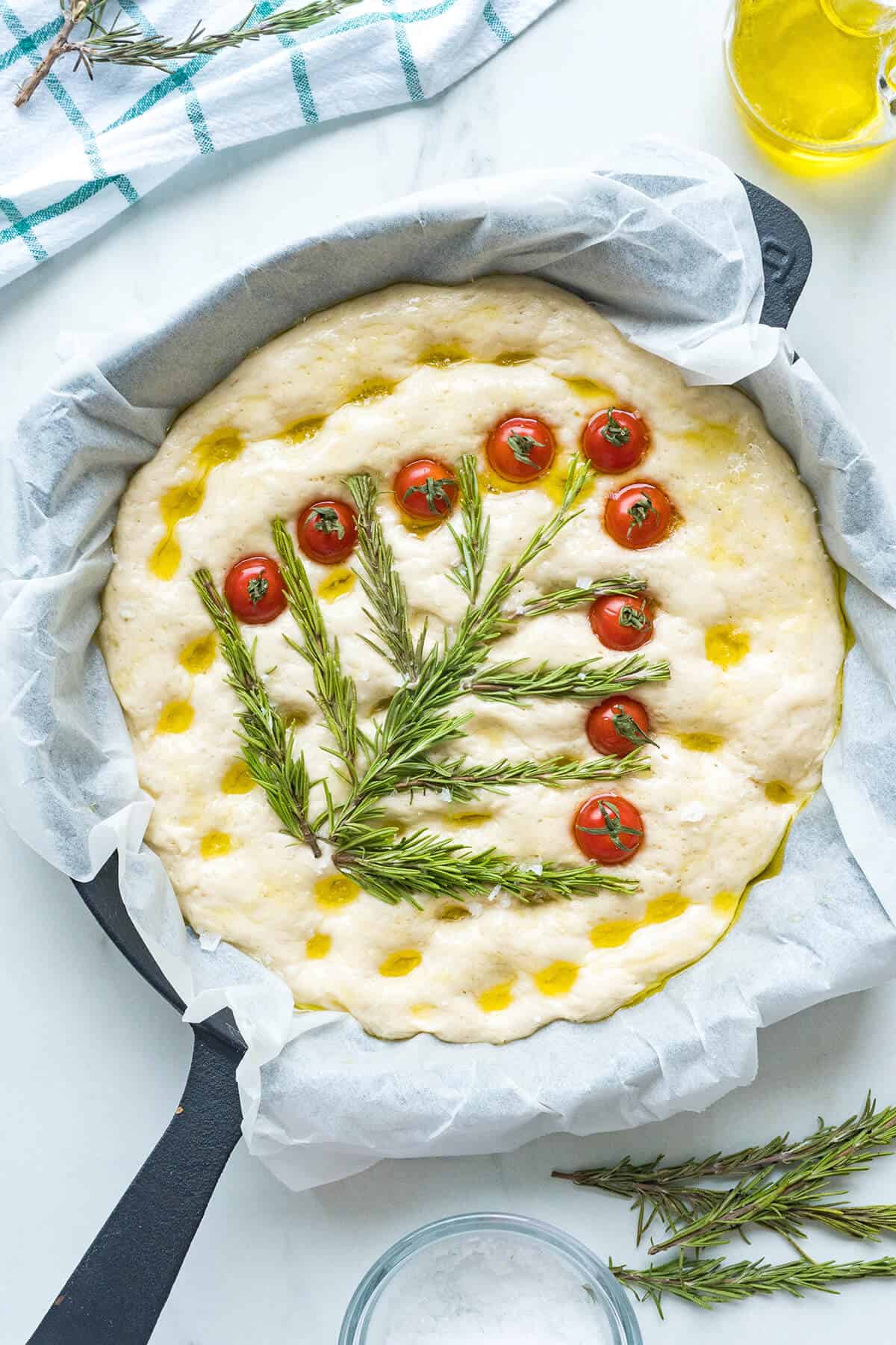 Creating a Christmas tree on the dough with rosemary sprigs and cherry tomatoes.