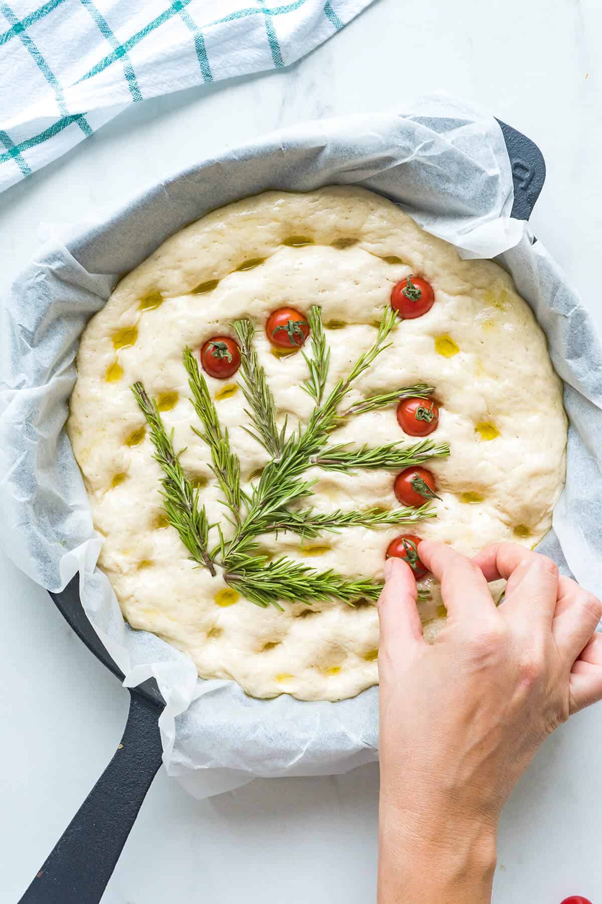 Creating a Christmas tree on the dough with rosemary sprigs and cherry tomatoes.