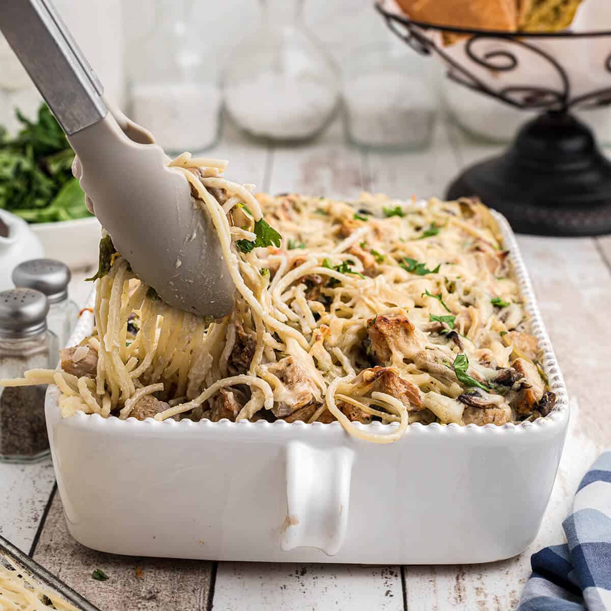 Turkey tetrazzini in a casserole dish with serving tongs.