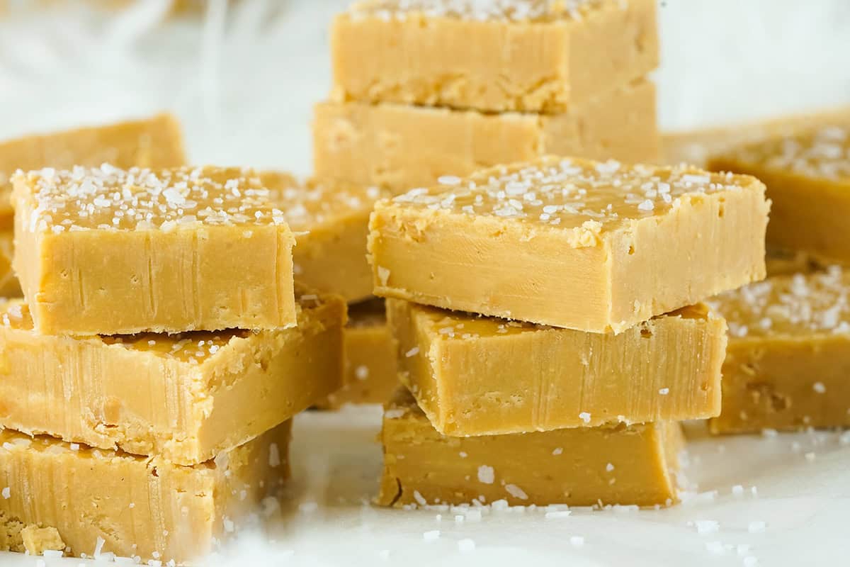 Close-up of stacked squares of creamy peanut butter fudge topped with coarse salt crystals.