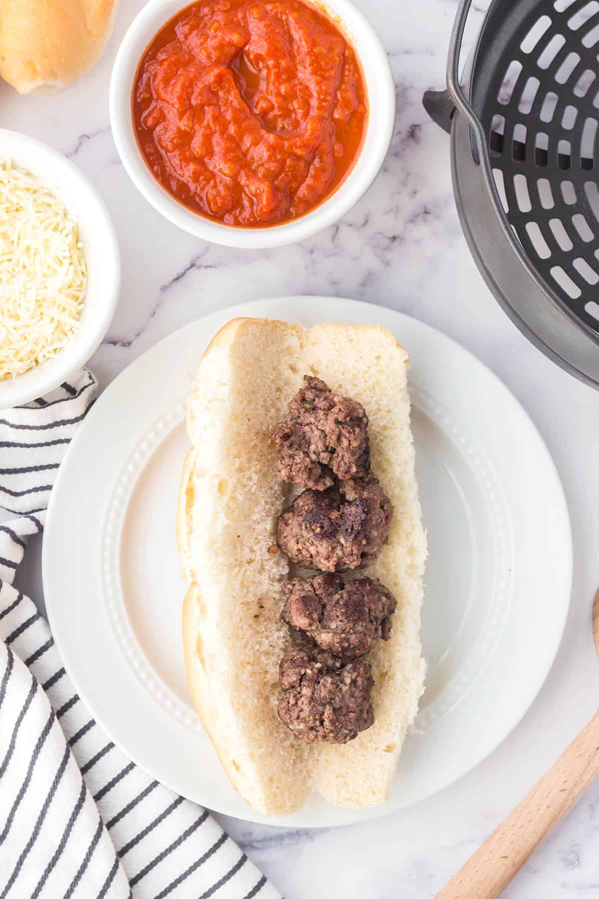 A split hoagie roll containing 3 meatballs on a white plate.