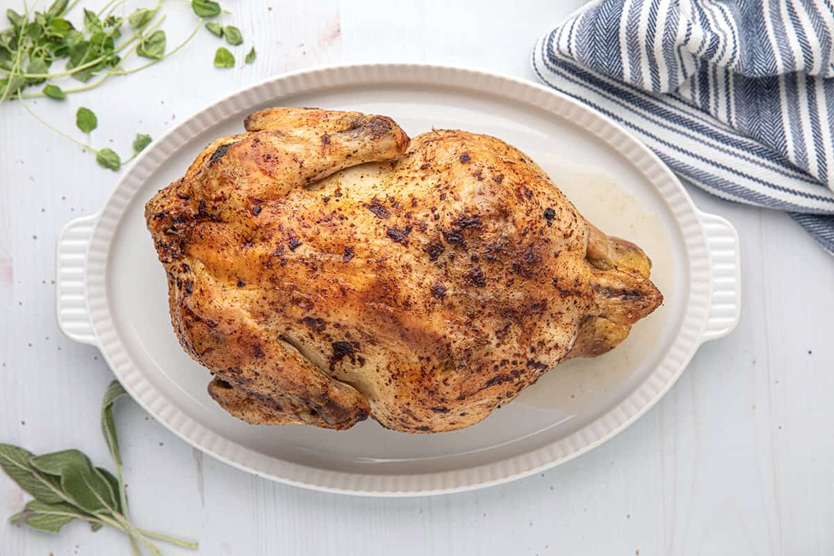 Whole roasted chicken on a white serving platter.