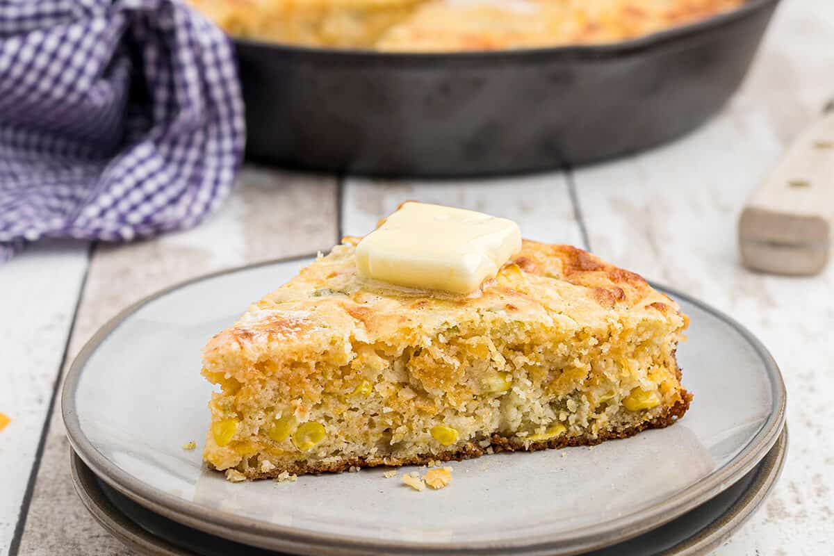 A slice of cornbread with a pat of butter on top on a serving plate.