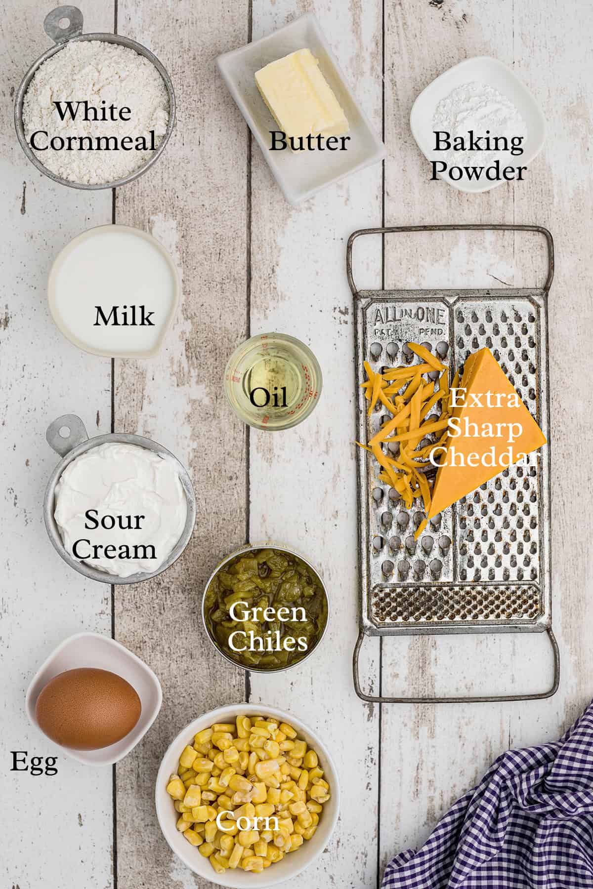 Ingredients for cornbread, including cornmeal, butter, baking powder, cheese, oil, milk, sour cream, chiles, corn, and egg.