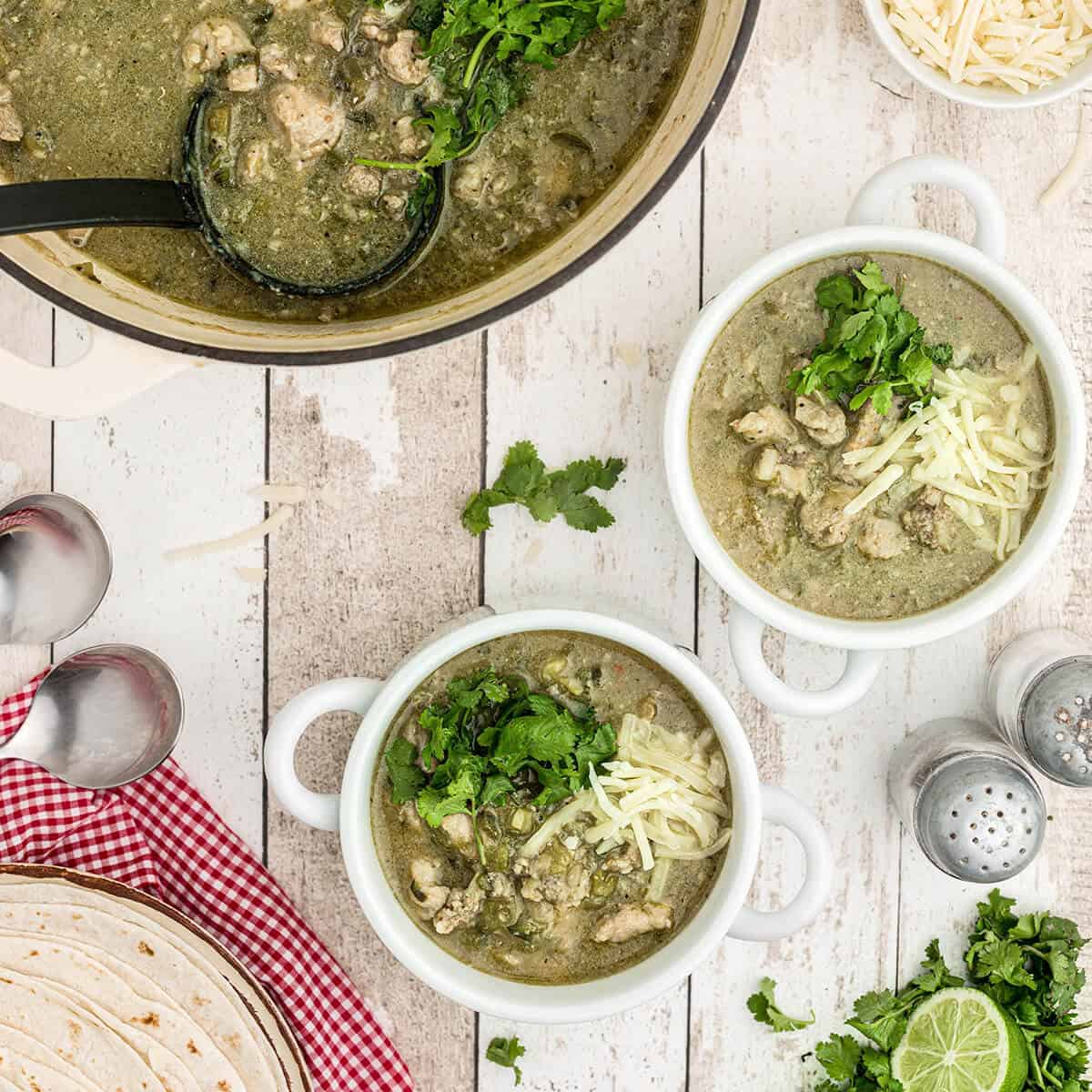 Servings of chili verde in white bowls garnished with cheese and cilantro.