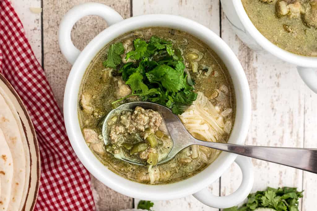 A serving of chili verde in a white bowl garnished with cheese and cilantro.