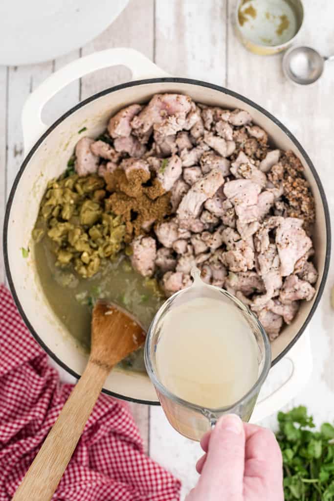 Adding chicken stock to ingredients in a Dutch oven.