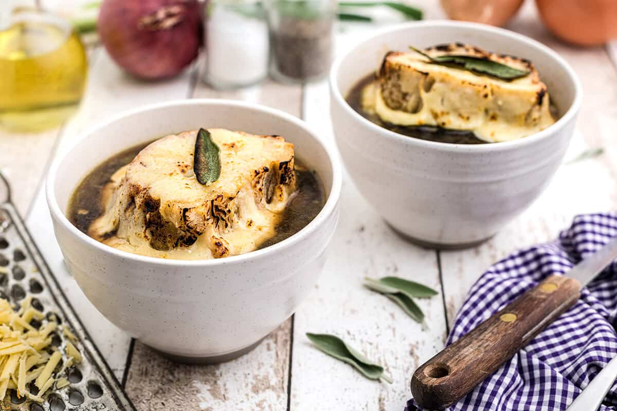English onion soup in white bowls on a wooden background.