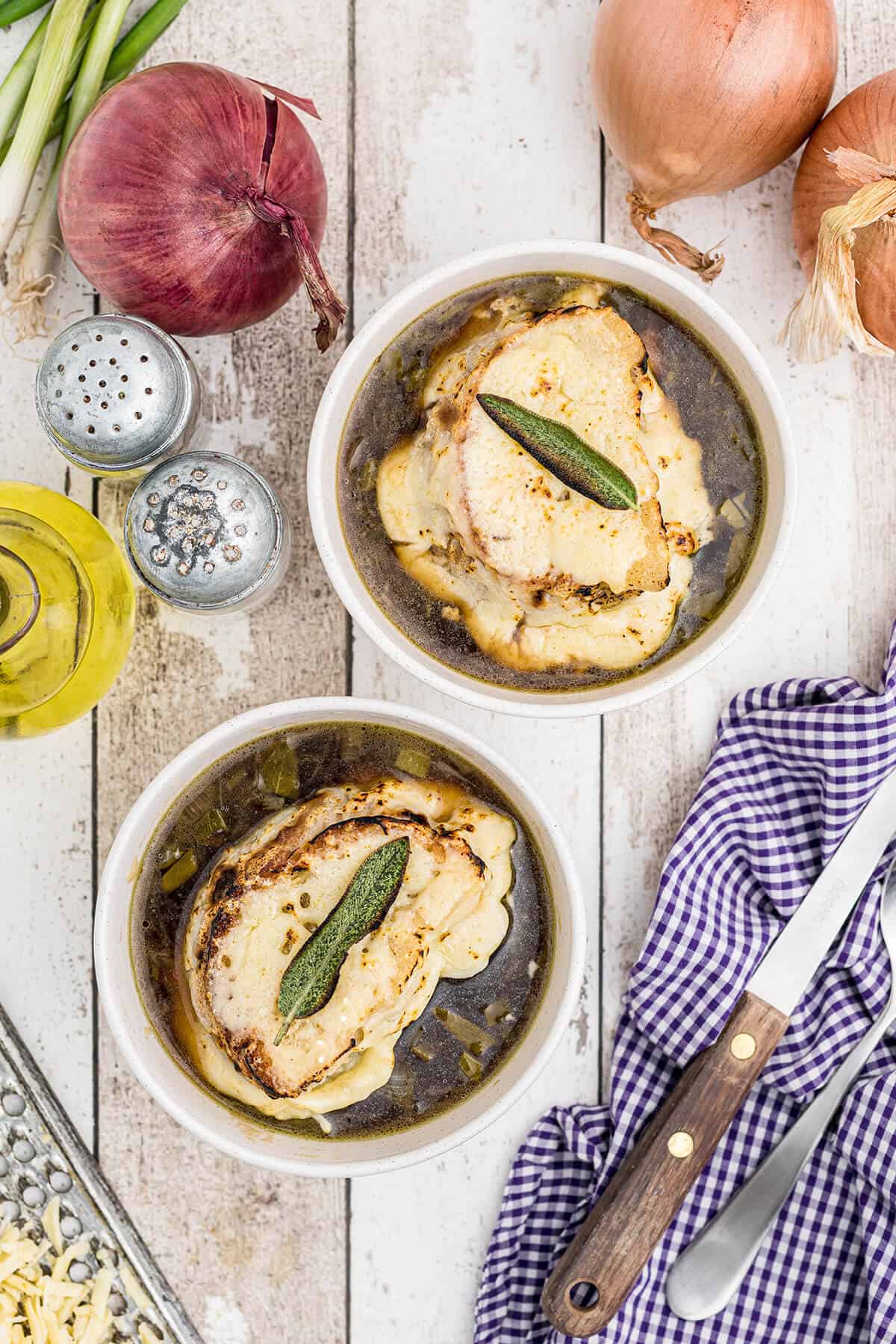 Finished soup in bowls topped with toast, melted cheese, and sage leaves.